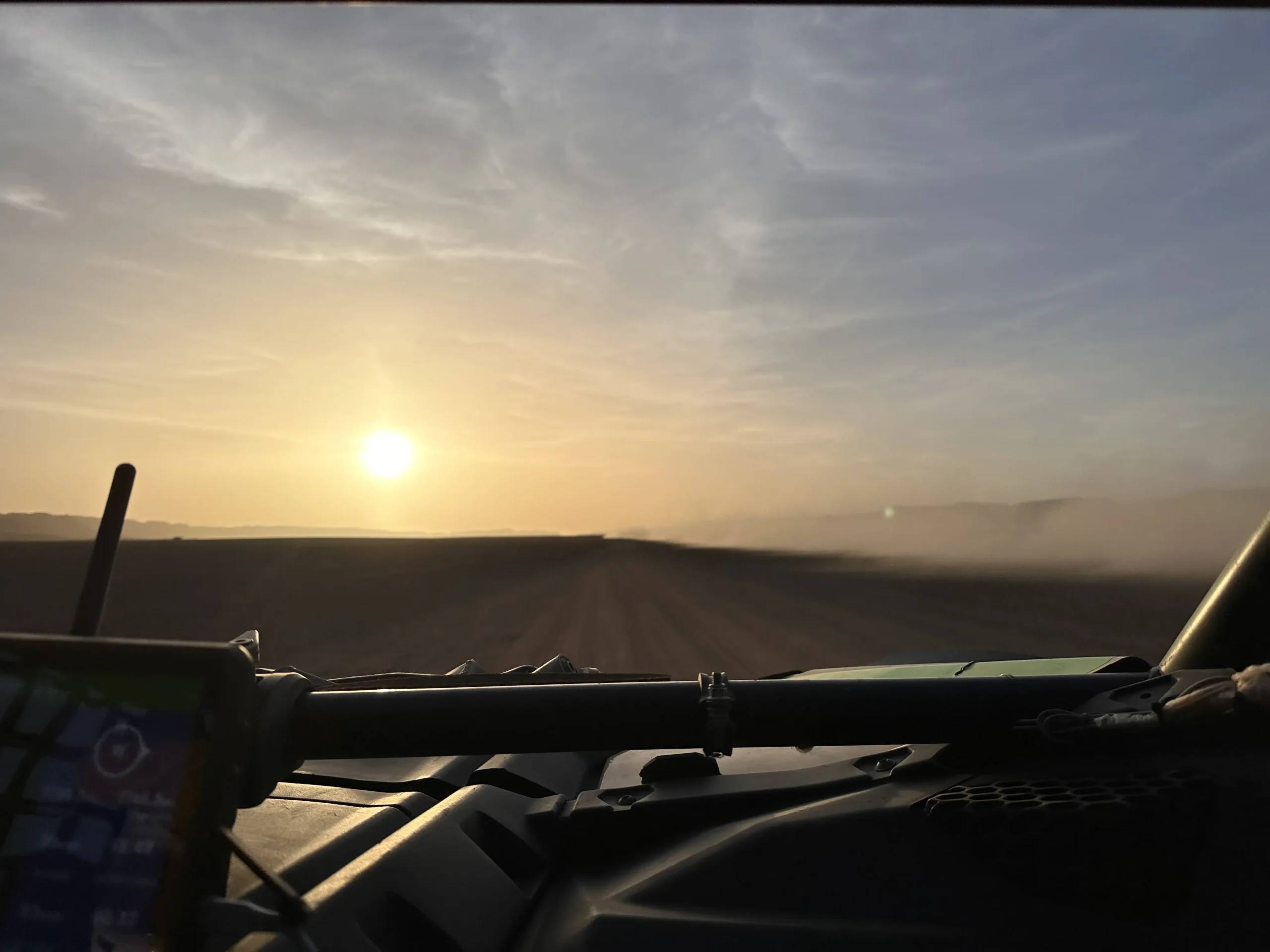 Widok z wnętrza pojazdu UTV na piaszczystą drogę o zachodzie słońca podczas wyprawy off-road.